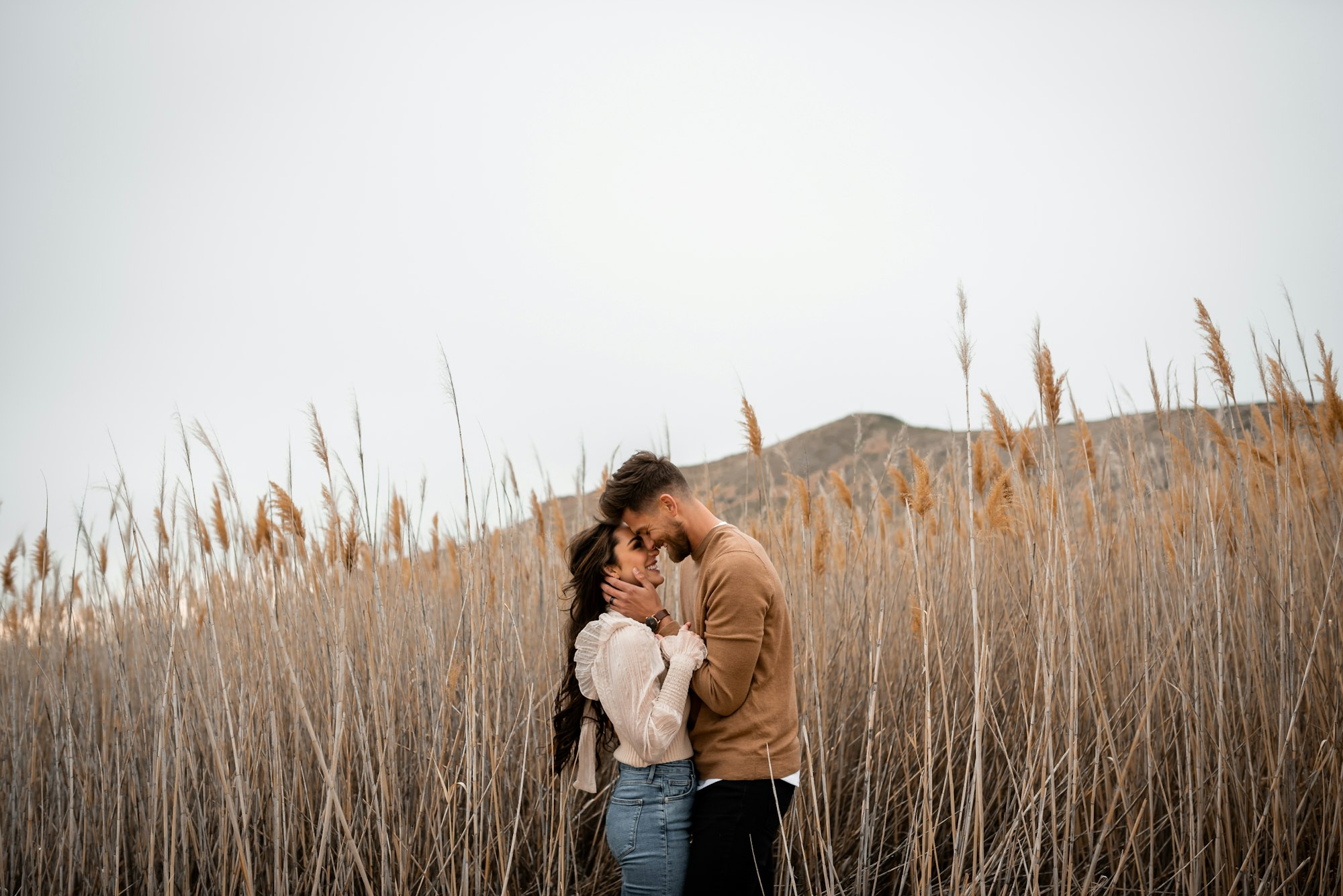 A couple holding each other in a field of tall golden grass at golden hour